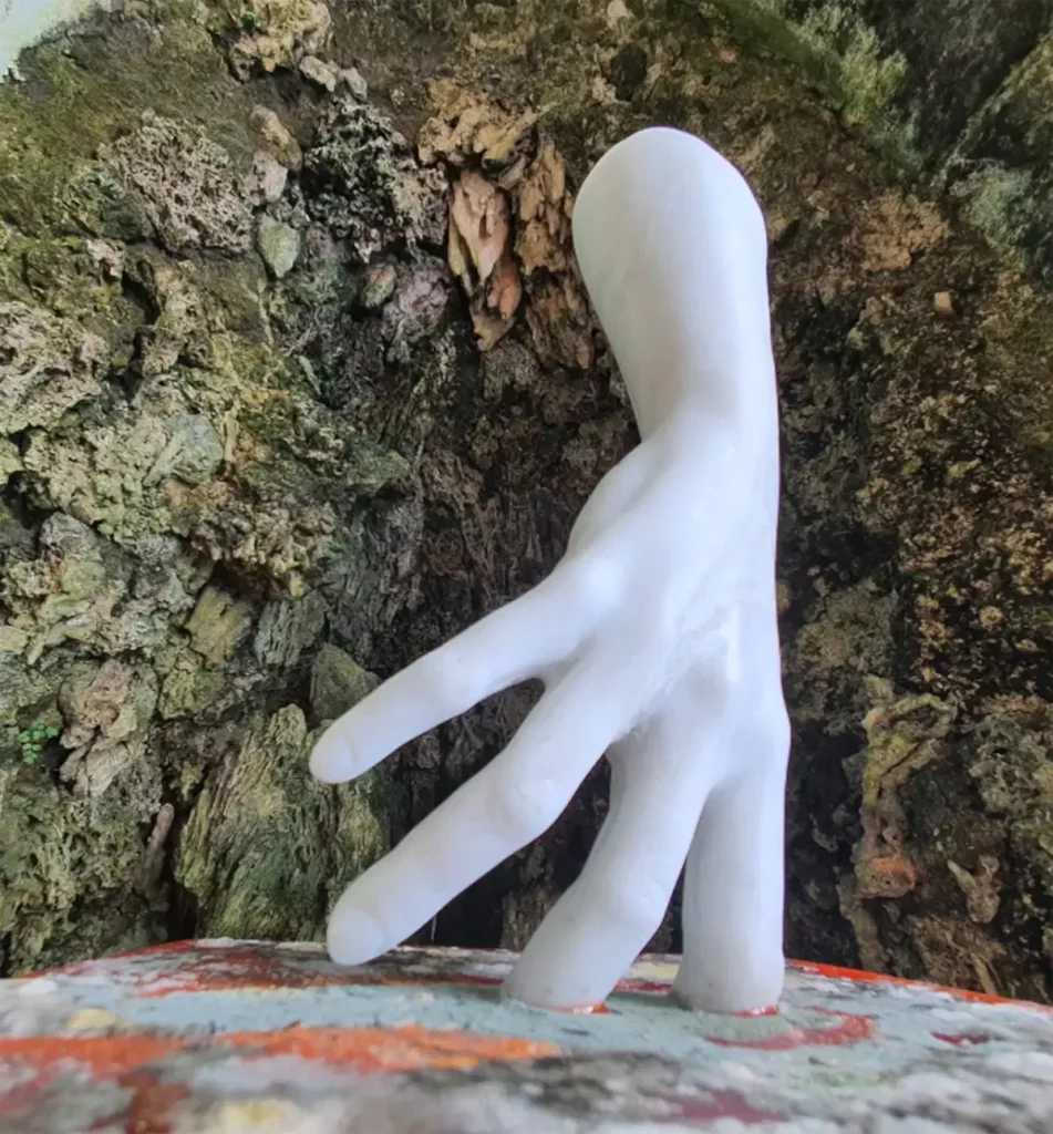 White hand sculpture reaching forward from a rough, rocky wall surface.