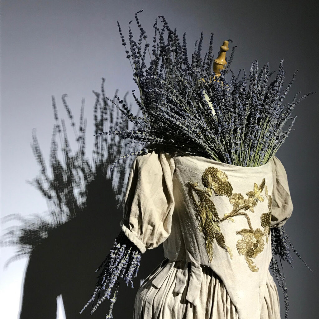 00 - Lambda Biologics - Lambda Biologics Lavender bouquet tucked into a cream dress with gold embroidery, seen in a close-up.