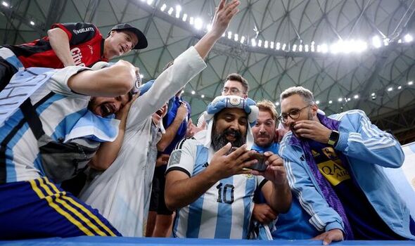 Group of Argentina soccer fans in blue-and-white jerseys crowding around to take a selfie in the stadium.