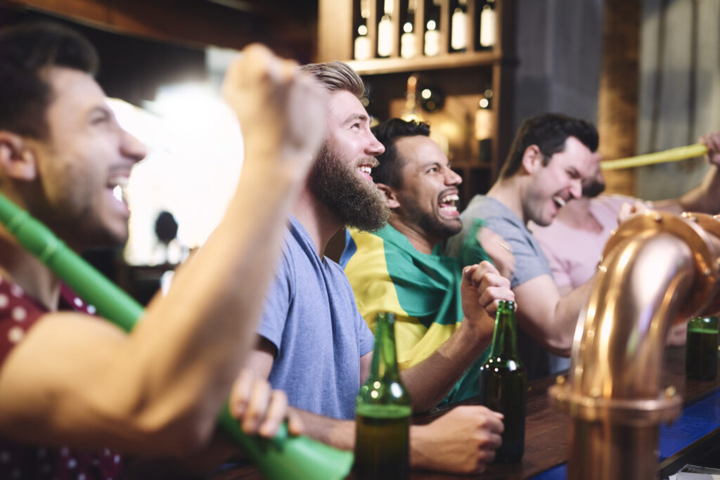 Happy men while watching american football - Lambda Biologics - Lambda Biologics Group of friends at a bar raising beer bottles and cheering together at a lively pub.