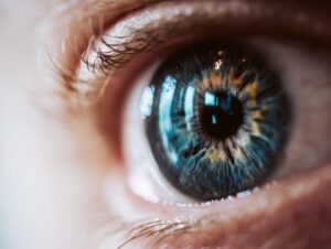Close up of a human eye showing a blue green iris pupil and surrounding eyelashes with reflections on the cornea